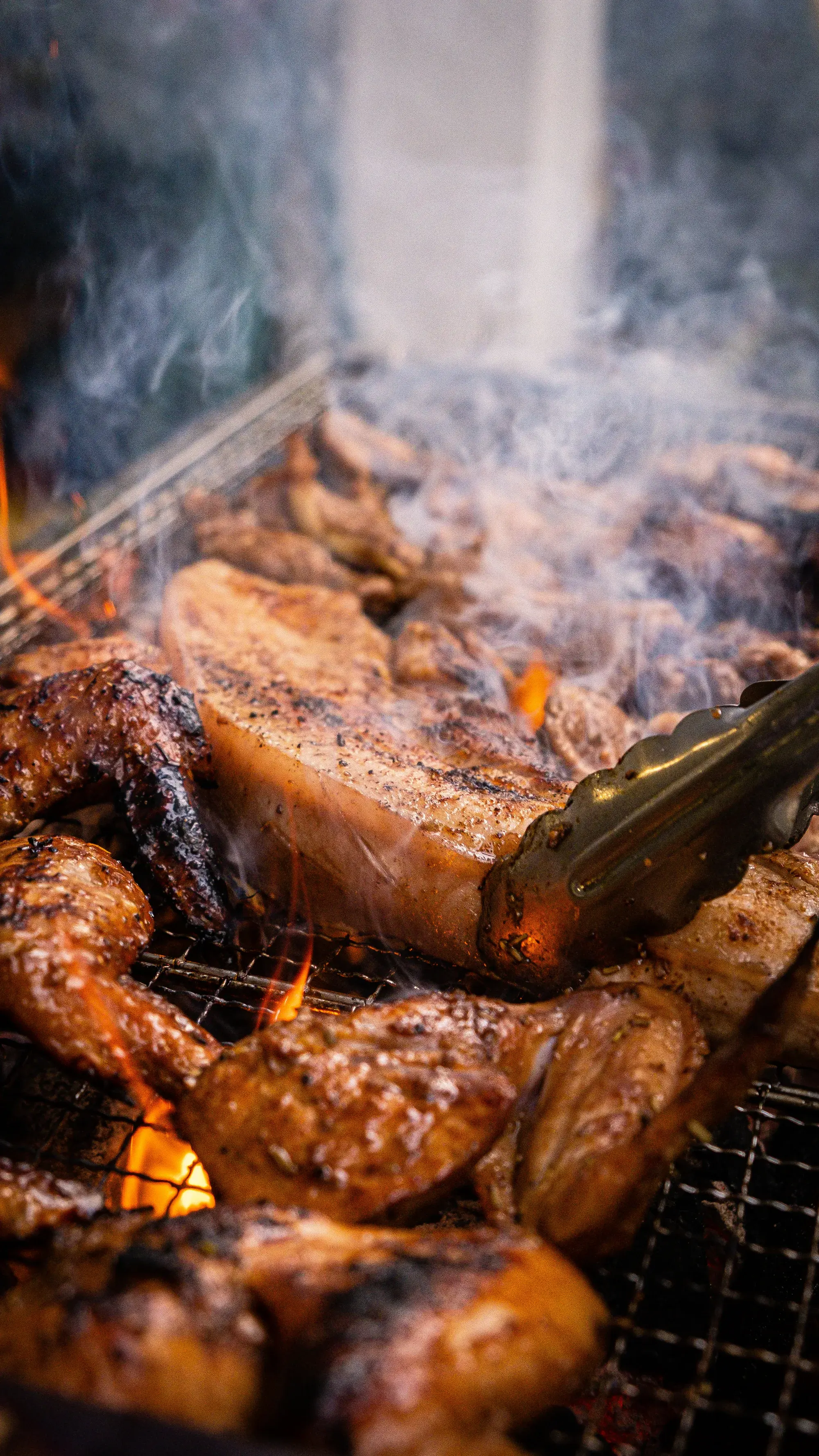 Chicken and pork over a live charcoal fire, smoke rising off the grill