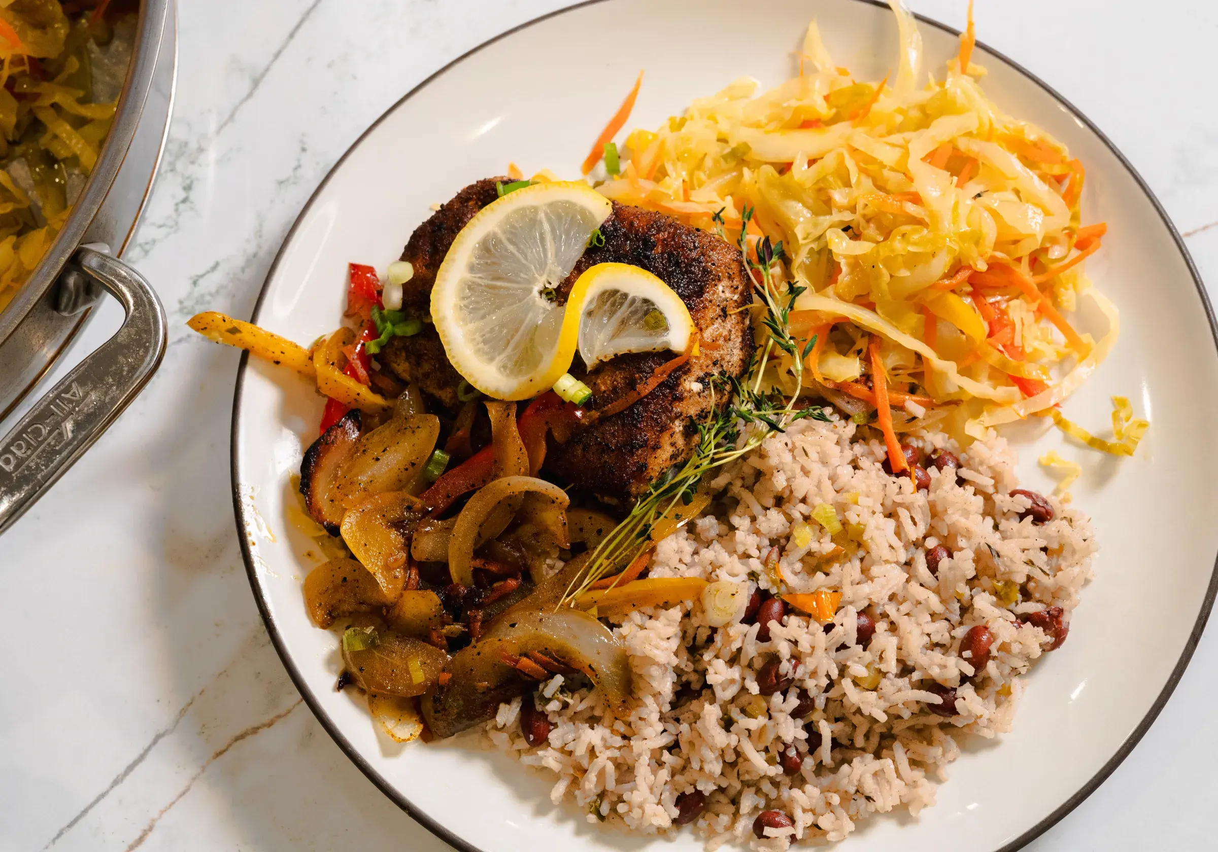 A plated meal of blackened fish, rice and peas, steamed cabbage and peppers